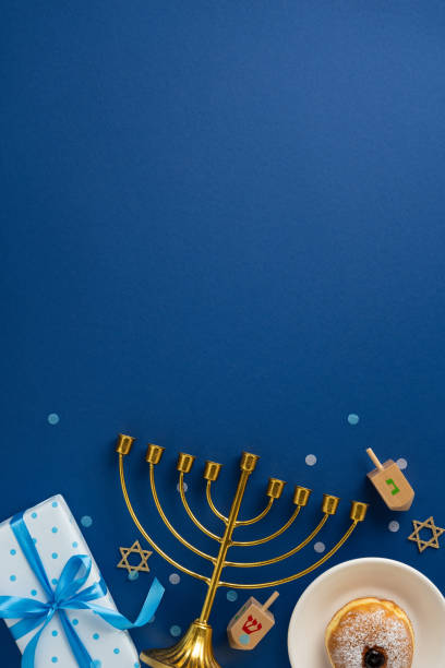 istock A festive vertical Hanukkah scene featuring a golden menorah, dreidels, a wrapped gift, and a traditional donut on a dark blue background 2182505539