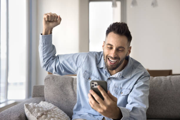 istock Happy overjoyed handsome Hispanic man using mobile phone at home 2182505859