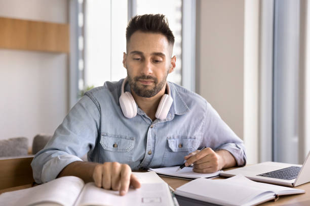 istock Focused adult Latin student man reading learning textbook at home 2182507107