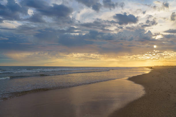istock Golden sunset casts a warm glow over gentle waves and a cloudy sky. 2182511993