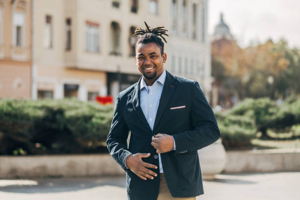 istock Confident, smiling black businessman with dreadlocks in casual blazer standing outdoors on sunny day in urban setting, looking at camera 2182516446