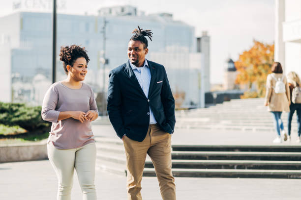 istock Two people walking together in a city environment, smiling and engaged in conversation, with modern buildings in the background 2182516509