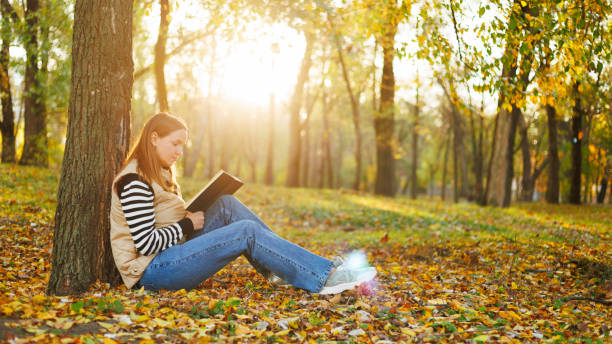istock Woman reading book in autumn park 2182525080