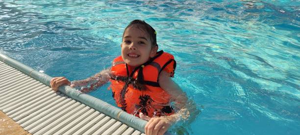 istock Child wearing life jacket smiling in pool on sunny day 2182531227