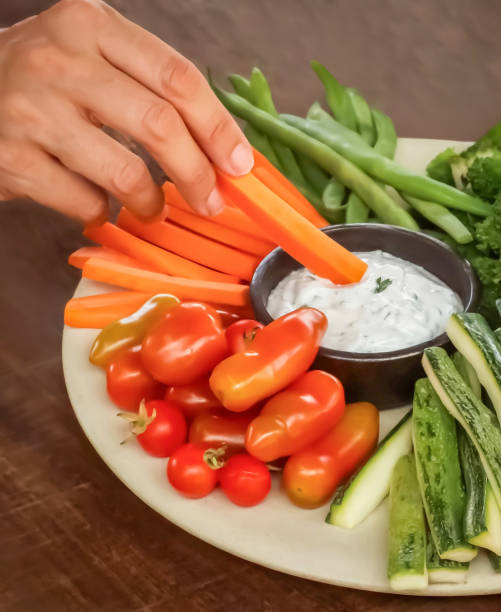 istock Hand Dipping Carrot Stick in Yogurt Dip with Fresh Vegetables 2182531591