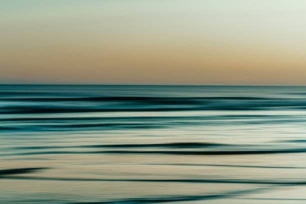 istock Blurred ocean waves in soft green and orange hues during twilight. 2182532642