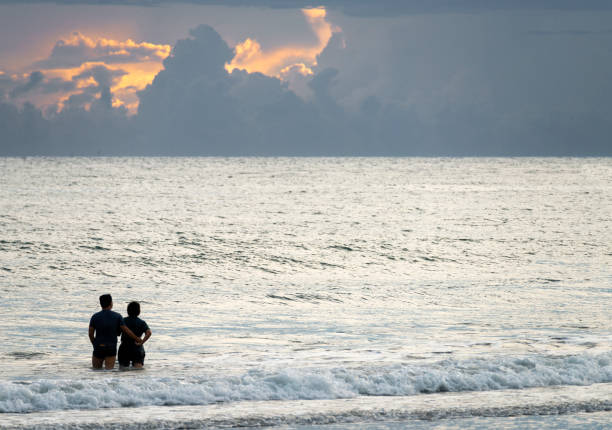 Luzon Island,The Philippines-May 22 2023:Two human figures walk into the sea,gentle tropical waves lapping the quiet sands,and a warm offshore breeze ,at sundown.