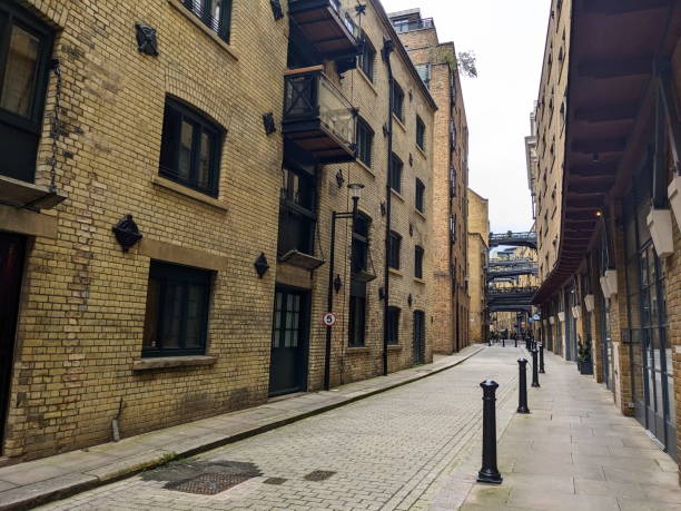 London, UK - 05.13.2024: A quiet time of Shad Thames with converted warehouses and elevated walkways over the tiled floor and shops on the ground floor under a cloudy sky without tourists