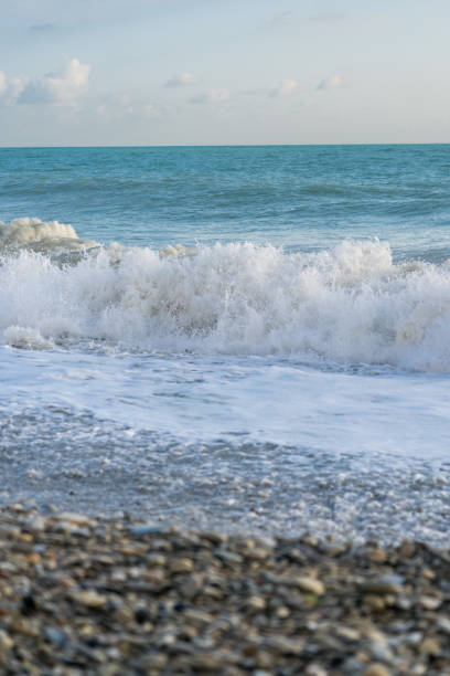 istock The sea waves roll onto a pebble sea shore against a blue sky with clouds. 2182551380