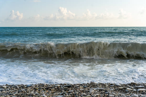 istock The sea waves roll onto a pebble sea shore against a blue sky with clouds. 2182551441