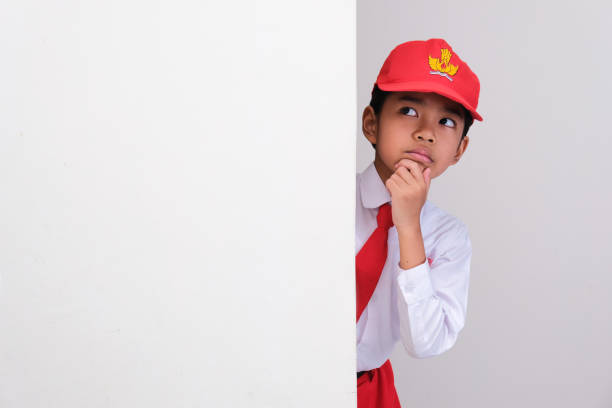 Indonesian school student peeking from behind a wall showing thinking face