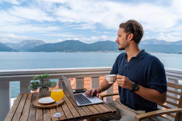 istock Young entrepreneur doing remote work from the balcony by the sea and enjoying the views 2182564020