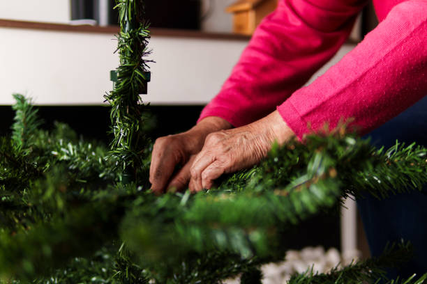 A woman is decorating a Christmas tree with green branches