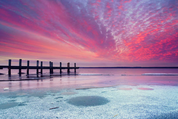 cold winter landscape with ice and snow, amazing sunset light over an old wooden pier with frozen sea
