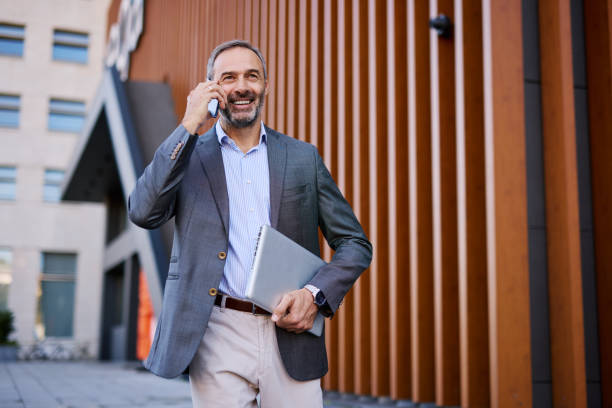 istock Confident Businessman Talking on Phone Holding a Laptop 2182599247