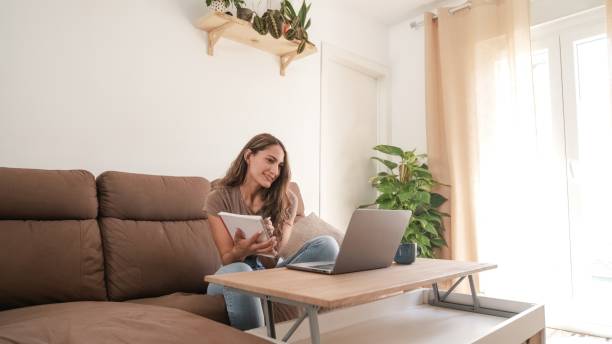 istock Happy woman writing in diary while working on laptop at home 2182606329