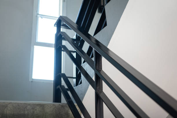 Abstract view of a blue metal spiral staircase with sunlight casting geometric shadows and reflections on the ground below.