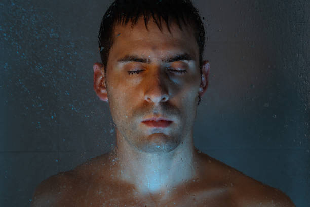 A man under the water of the shower with a serious face, affected. He seeks to disconnect and keep stress and anxiety under control.