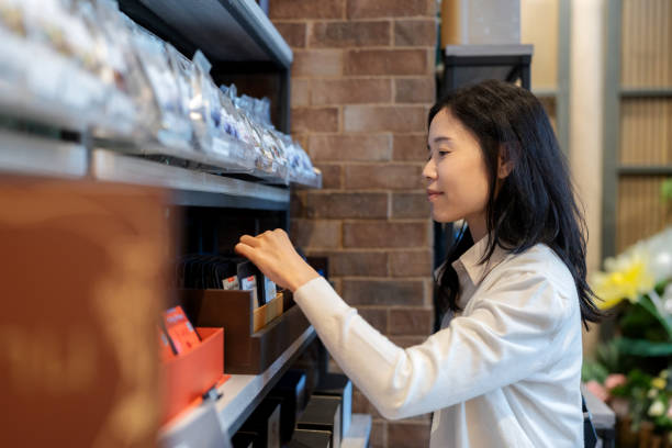 A customer in relaxed attire explores a range of coffee bean options on display, thoughtfully choosing the perfect blend from neatly packaged selections on a coffee shop shelf, radiating confidence and enjoyment in her choice.