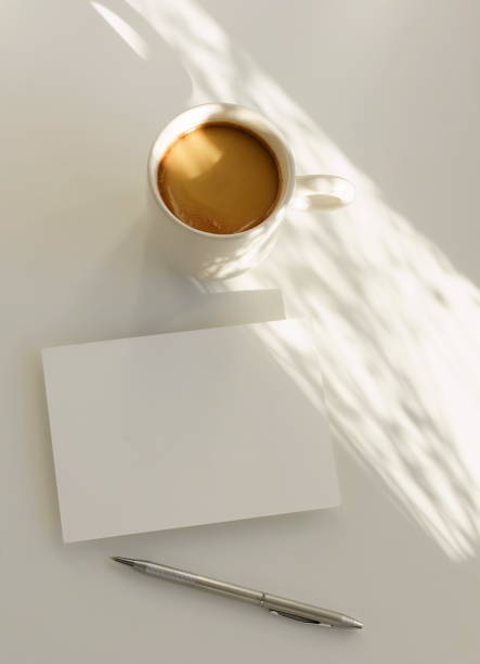 Card blank mockup with copy space and coffee cup with sunlight shadow top view on white background. Minimalist still life concept.