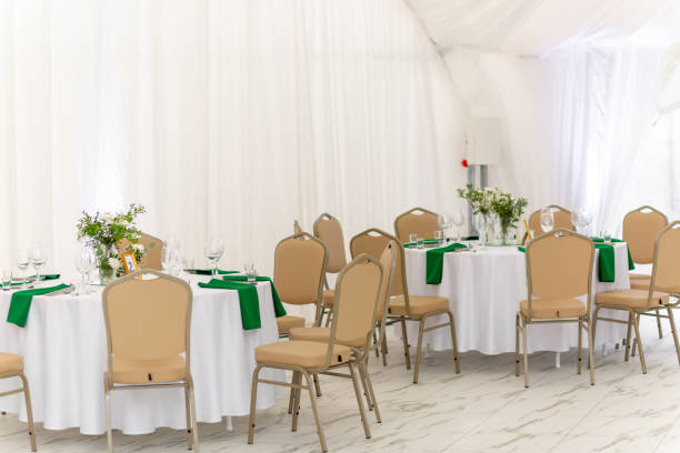 istock Wine glasses, silver tableware and green napkins on round tables covered with white tablecloth. 2182620412