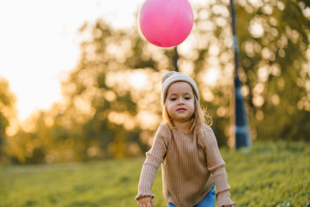 A cute little girl is playing with a balloon in the park during an autumn day