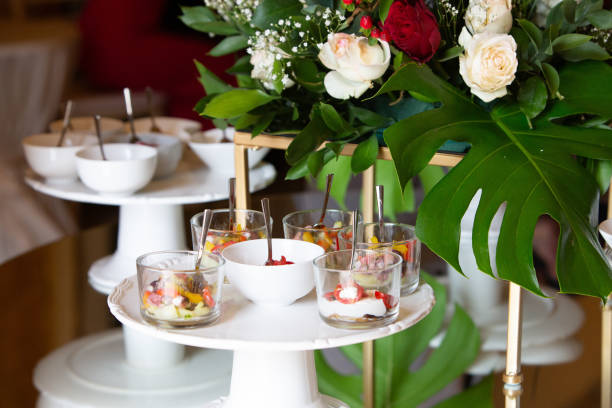 Small snacks and appetizers served on cake stands at a banquet, decorated with flowers and monstera leaves