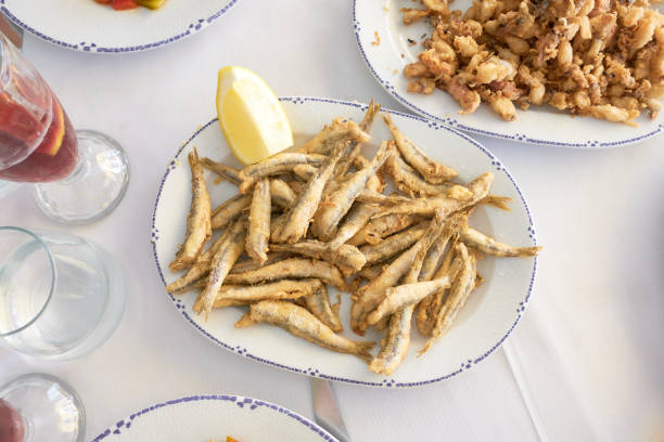 Top view of traditional Spanish fried fish dishes like whitebait or small anchovies with fresh lemon wedges, ready to share on a white tablecloth setting
