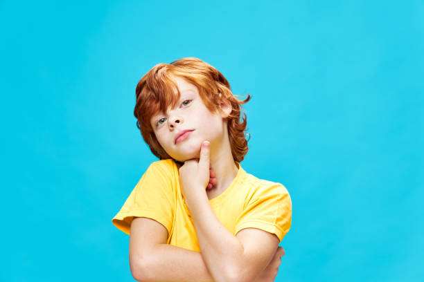 istock redhead boy holding hand near face tilting head to one side blue isolated background 2182634459