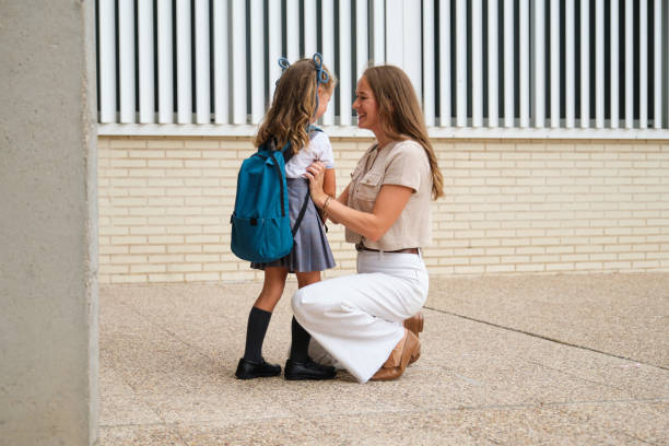 Caring mother preparing her daughter for school, adjusting her backpack and talking to her