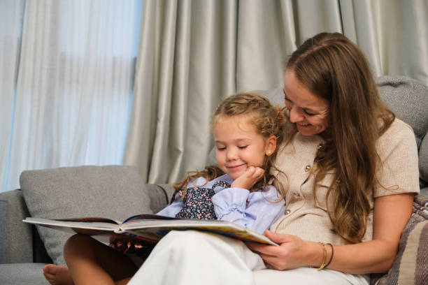 istock Mother and daughter reading a book together on sofa at home 2182648010