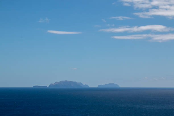 Calm water of Atlantic ocean. Small islands belonging to Madeira on the horizon. Blue sky with white clouds. View from Vulcao Penha de Aquia, Madeira, Portugal.