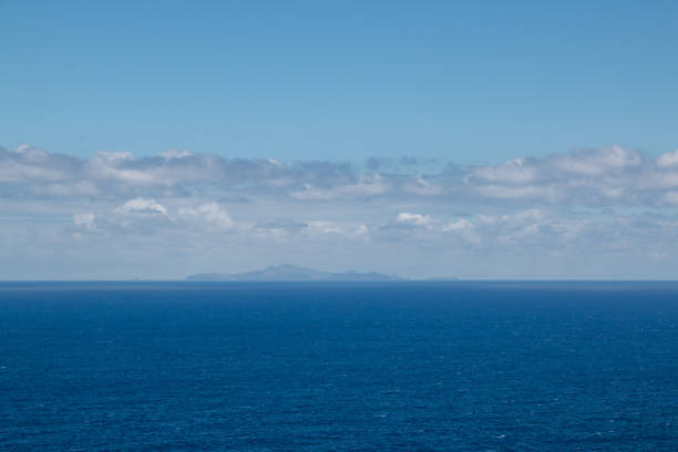 Calm water of Atlantic ocean. Small islands belonging to Madeira on the horizon. Blue sky with white clouds. View from Vulcao Penha de Aquia, Madeira, Portugal.