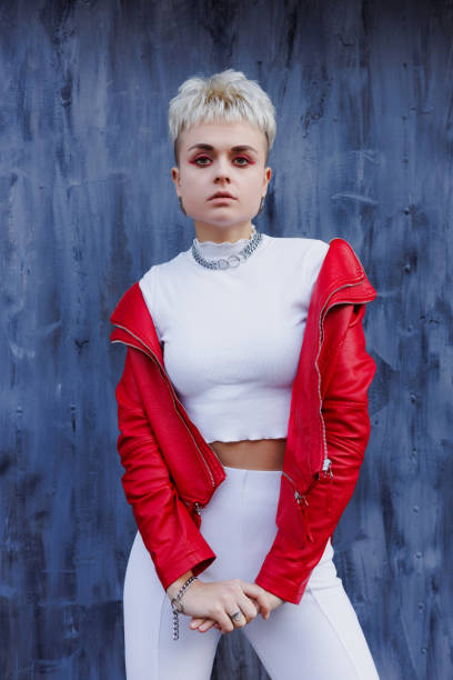 istock Modern woman in white outfit and red leather jacket looking at camera on textured blue background 2182667892
