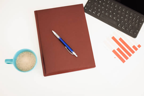 Close up view of desk workplace with notebook, pen, laptop, and paperwork or report
