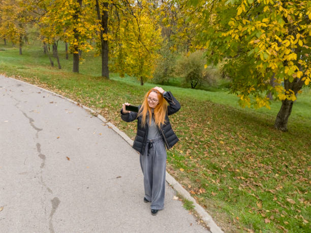 Woman walking in public park and taking selfies with beautiful autumn color trees in background