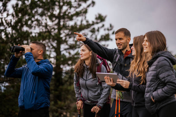 A group of hikers navigates the trail using a tablet while exploring a scenic outdoor setting surrounded by trees