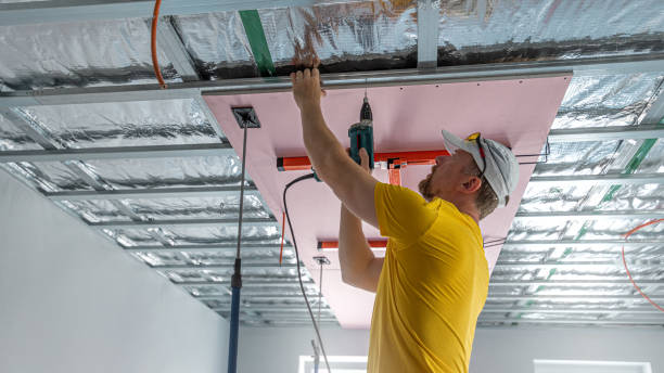 istock The worker screwing plasterboard to the ceiling. He is using special electric screwdriver and drywall lift. A red plasterboard improve the fire resistance of ceiling structures. 2182703655