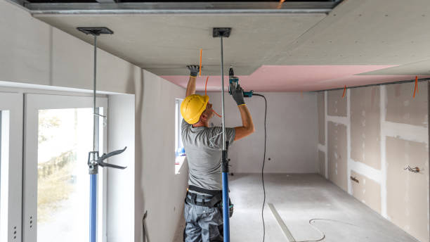 istock The worker screwing plasterboard to the ceiling. He is using special electric screwdriver and drywall lift. A red plasterboard improve the fire resistance of ceiling structures. 2182704724