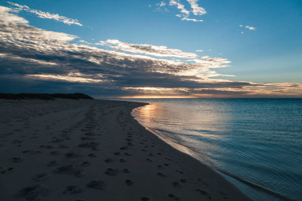 The vibrant sunset casts a warm glow over the tranquil waters, with gentle waves lapping at the sandy beach, revealing a serene landscape at Cape Range National Park in Western Australia.