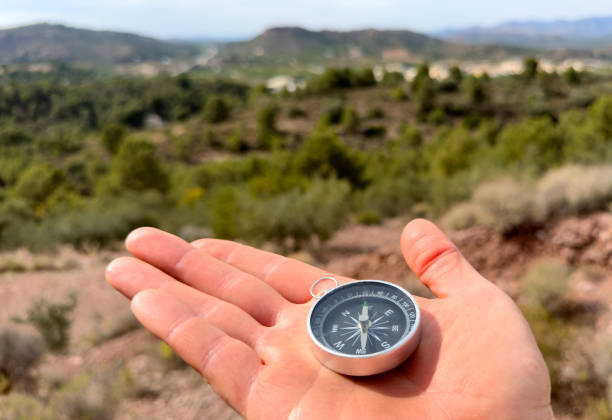Compass in hand in mountains during Hiking. Tourist compass for orientation on terrain. Magnetic declination alculator. Map reading and land navigation concept. Orient on maps in Spain mountains.