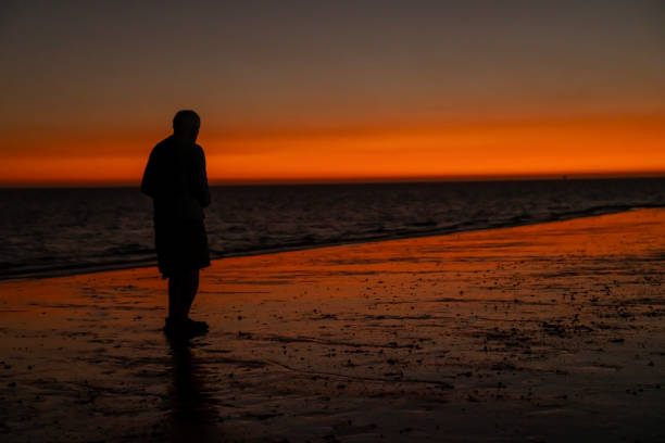 Silhouette of a man on a wet sandy beach in front of a dramatic sunset sky. Madagascar