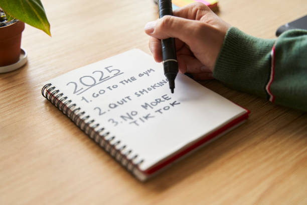 istock New year's resolutions. Hand starting 2025 goals indexed list in notebook 2182715425
