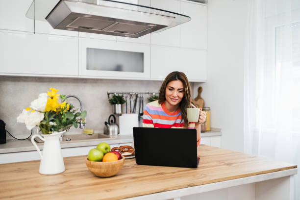 istock A young woman uses a mobile phone reading the latest news while preparing for breakfast 2182718533