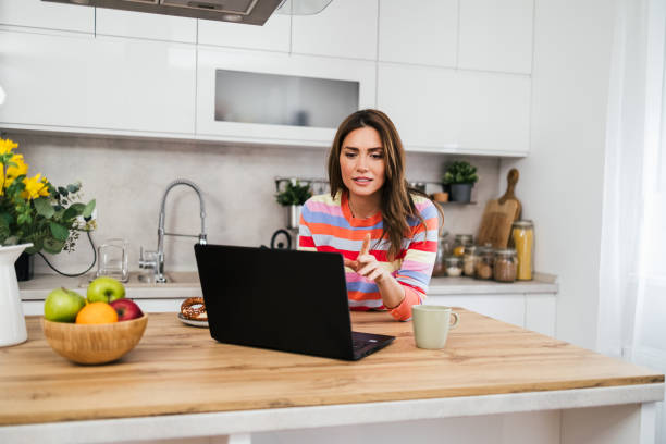 istock A young woman uses a mobile phone reading the latest news while preparing for breakfast 2182718559