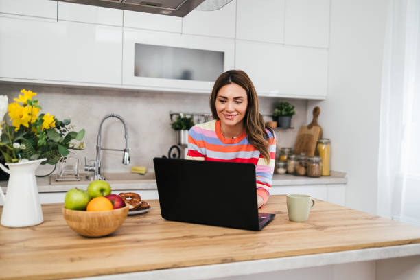 istock A young woman uses a mobile phone reading the latest news while preparing for breakfast 2182718595