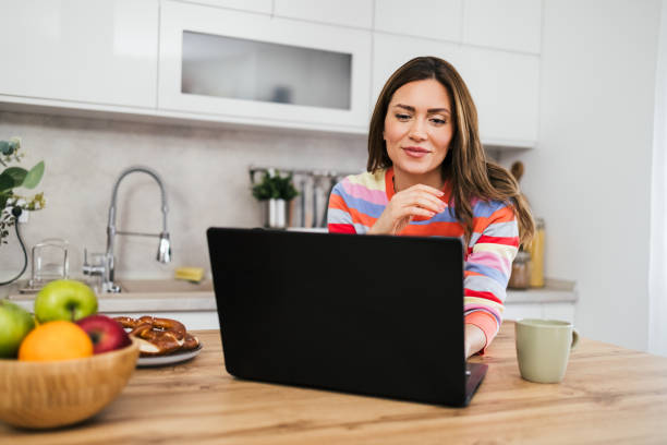 istock A young woman uses a mobile phone reading the latest news while preparing for breakfast 2182718741