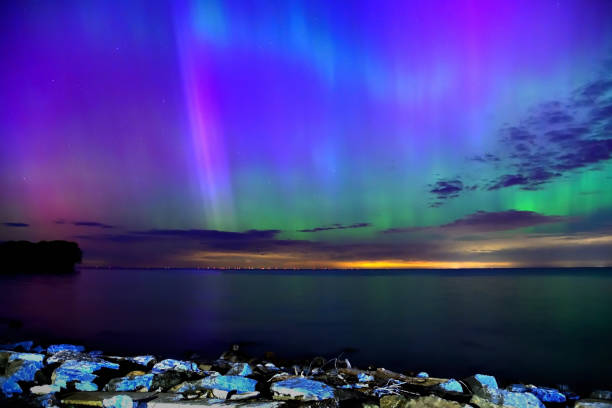 Northern lights over lake, rock foreground, long exposure, purple sky, green hues
