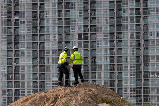 A low-angle view shows two engineers inspecting the progress of a new residential construction project. They are ensuring that everything is in order before proceeding to the next stage. Their goal is to identify any potential issues early and ensure the project runs smoothly as they work on building this new community.