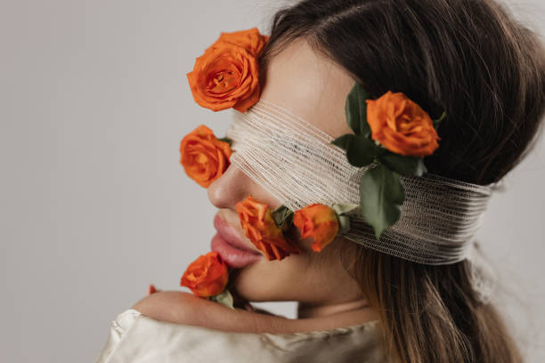 Portrait of a beautiful young woman having covered eyes with roses and cotton bandage, studio shot in front of white background